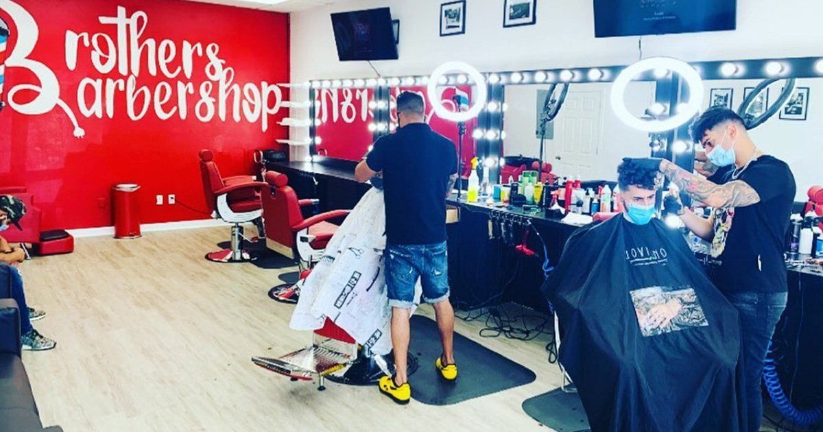 Inside Brothers Barbershop — barbers at work by the red logo wall